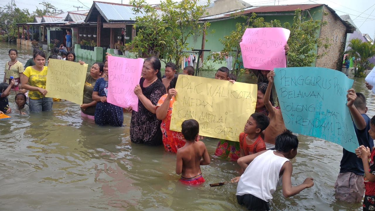 Berita Sore/Andi Aria Tirtayasa Kaum ibu dan anak-anak memperlihatkan sejumlah poster saat melakukan aksi unjuk rasa di tengah-tengah genangan banjir yang melanda Komplek Perumahan Buruh TKBM Upaya Karya Pelabuhan Belawan Kelurahan Sei Mati Kecamatan Medan Belawan, Senin (21/11).