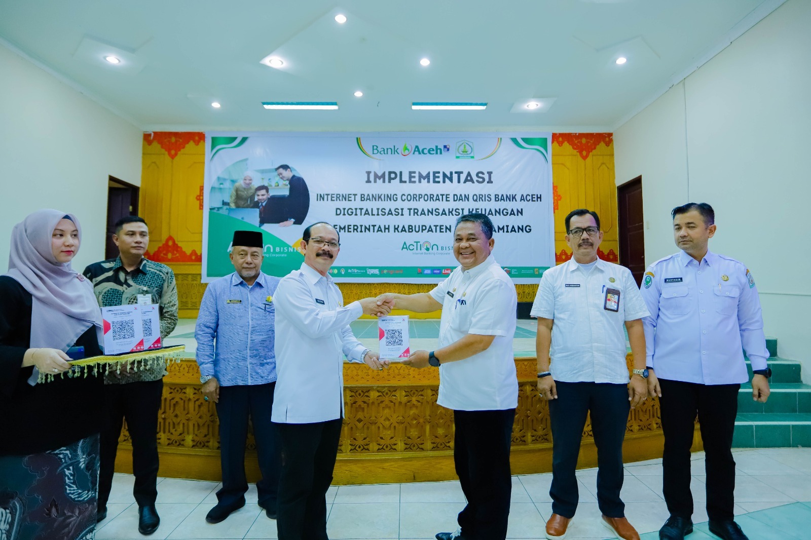 Teks Foto : Penjabat (Pj) Bupati Kabupaten Aceh Tamiang, Dr. Drs. Meurah Budiman, SH, MH secara simbolis menyerahkan kode QRIS Internet Banking Corporate kepada Sekretaris Daerah Drs. Asra saat launching implementasi digitalisasi transaksi keuangan bersama Bank Aceh Syariah.
