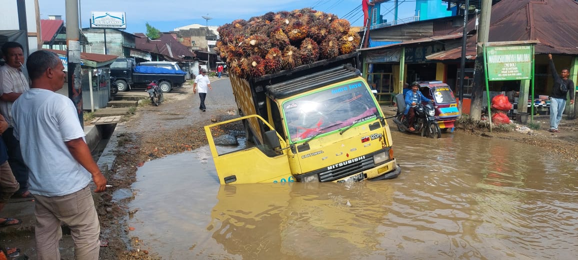 Truk bermuatan TBS Sawit terperosok di jalan rusak, lubang bak kubangan di badan jalinsum di sekitar pasar Ujung Batu kecamatan Sosa Kabupaten Padang Lawas, Rabu (15/11). (Foto: Idaham Butar Butar)